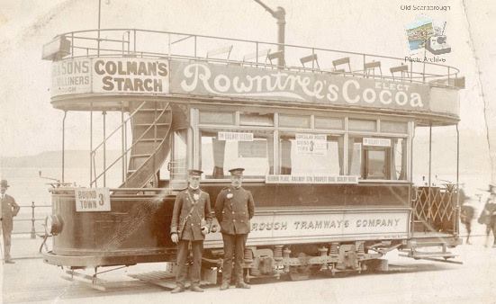 Two men stood in front of a local tram operated by the Scarborough Tramways Company, on the side there is an advertisement for Rowntrees Cocoa